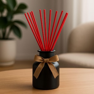 May include: A black aromatherapy diffuser with red reeds and a tan bow. The diffuser is a small, round bottle with a narrow neck. The reeds are long and thin, and they are arranged in a fan shape. The bow is made of a coarse fabric.