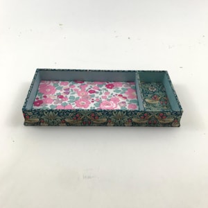 May include: A rectangular divided tray featuring a dark blue exterior with a botanical bird and berry pattern. The larger interior compartment is lined with a pink and white floral print, while the smaller section features a matching dark blue botanical pattern.