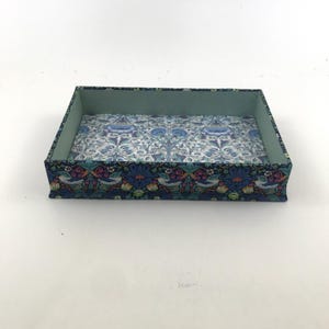 May include: Rectangular decorative tray with a floral pattern in shades of blue, teal, and white. The tray's interior is a light blue, and the exterior features a detailed design with birds and flowers. A stylish storage solution.