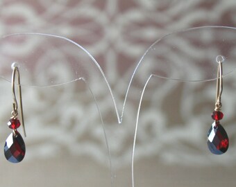May include: A pair of dangle earrings with a teardrop-shaped red gemstone and a smaller red gemstone above it.