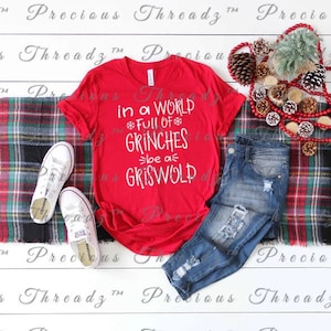 May include: Red t-shirt with a white graphic that says "in a world full of Grinches be a Griswold".