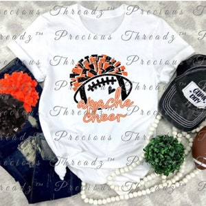 May include: A white t-shirt with a black and orange football graphic and the text "Apache Cheer". The graphic includes a football, a heart, and a black and orange pom-pom.