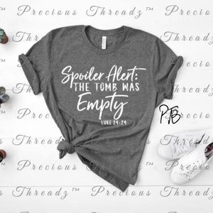 May include: A gray t-shirt with white text that reads "Spoiler Alert: The Tomb Was Empty" and "Luke 24:24".