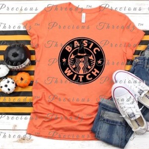 Peut inclure: T-shirt orange avec un graphique noir d'une sorcière portant un chapeau de sorcière et tenant une tasse de café. Le graphique a la forme d'un logo Starbucks et dit "Basic Witch".