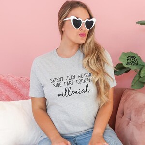 May include: A gray t-shirt with the text "Skinny Jean Wearin' Side Part Rockin' Millennial" printed in black.