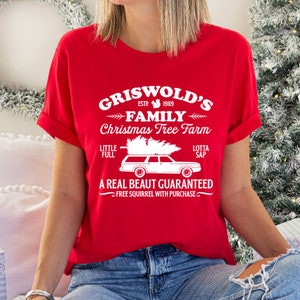 May include: Red t-shirt with white text that reads "Griswold's Family Christmas Tree Farm Est. 1989" with a cartoon image of a station wagon with a Christmas tree on top. The text also says "Little Full, Lotta Sap" and "A Real Beaut Guaranteed, Free Squirrel with Purchase."