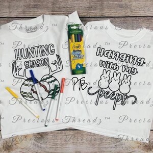 May include: Two white t-shirts with black outlines of Easter-themed designs. One shirt says "Hunting Season" with a deer head and two eggs. The other shirt says "Hanging with my Peeps" with three chicks. A pack of colored markers is included.