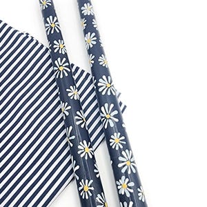 May include: Two navy blue taper candles decorated with white and yellow daisy flowers. A navy and white striped cloth is in the background. The candles are a decorative item.