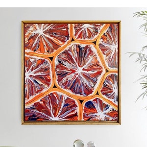 May include: Abstract painting of orange and white circles with a red and blue background. The painting is framed in gold and hangs on a white wall.