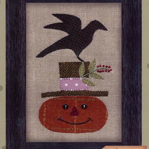 May include: Framed folk art piece titled "Happy Jack." The artwork features a smiling pumpkin wearing a hat, topped by a crow. The finished size is 5" x 7". The design is by Bonnie Sullivan.