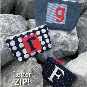 May include: Three zippered pouches featuring fabric appliques. One is blue with a white striped square and red letter g. Another is navy with white circles and a red square with a black letter r. The third is dark blue with a white letter F.