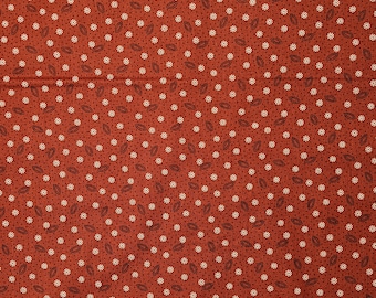 May include: A red fabric with a repeating pattern of small white flowers and dark brown leaves.
