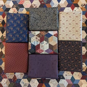 May include: A collection of eight fabric squares with various patterns, including floral, geometric, and paisley designs. The fabrics are in shades of blue, brown, red, purple, and cream.