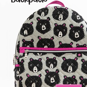 May include: A grey quilted backpack with a black bear print and pink accents. The backpack has a zipped pocket and a top handle. The text "Knot + Thread design" is printed on the front of the backpack.