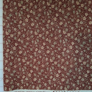 Könnte beinhalten: Nahaufnahme eines roten Stoffes mit einem kleinen weißen Blumenmuster. Der Stoff wird mit einem Lineal gemessen und der Text "GF5507R-15 Gentle Flowers" ist sichtbar.