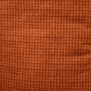 May include: Close-up of a textured fabric with a houndstooth pattern. The fabric is a warm, earthy brown color, with a repeating pattern of small, dark brown checks. The texture appears soft and possibly woven.