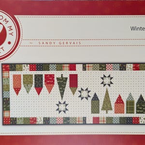 May include: A quilting pattern for a table runner featuring a winter village theme. The pattern is called "Winter Village" and is number #811. The pattern is by Sandy Gervais and is part of the "Pieces From My Heart" collection.