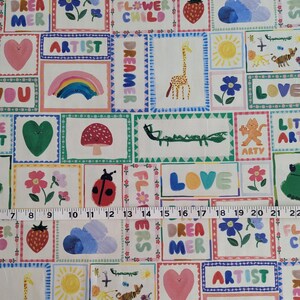 May include: A colorful fabric with a patchwork design featuring various illustrations and text. The illustrations include a giraffe, a ladybug, a rainbow, a flower, a sun, a heart, a cloud, a caterpillar, a frog, and a tiger. The text includes "LOVE", "DAY DREAMER", "ARTIST", "DREAMER", "FLOWER CHILD", "LITTLE ART", "LOVE YOU", and "FL#WERS".
