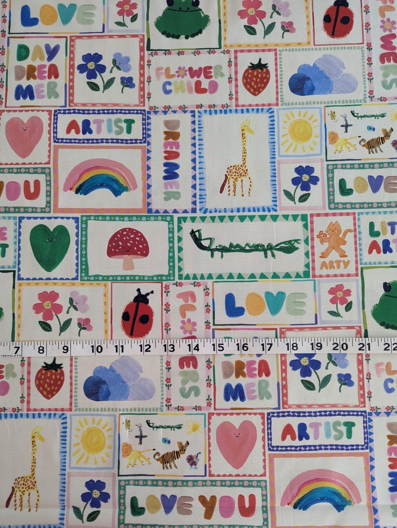 May include: A colorful fabric with a patchwork design featuring various illustrations and text. The illustrations include a giraffe, a ladybug, a rainbow, a flower, a sun, a heart, a cloud, a caterpillar, a frog, and a tiger. The text includes "LOVE", "DAY DREAMER", "ARTIST", "DREAMER", "FLOWER CHILD", "LITTLE ART", "LOVE YOU", and "FL#WERS".
