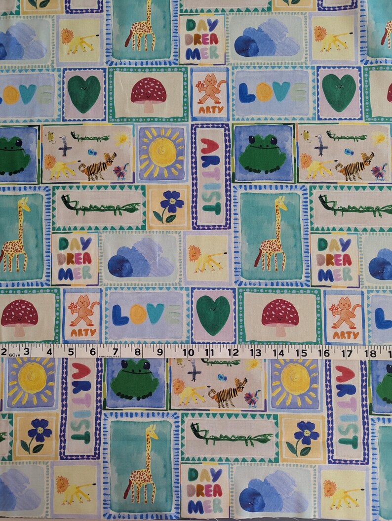Op de afbeelding: Een kleurrijke stof met een herhalend patroon van vierkanten. Elk vierkant bevat een andere illustratie, waaronder een giraffe, een kikker, een paddenstoel, een hart, een zon, een wolk en de woorden "Day Dreamer", "Artist" en "Love".