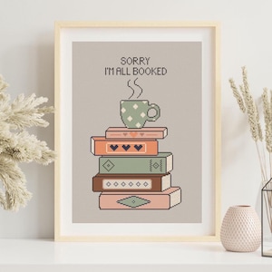 May include: A framed cross-stitch design with a stack of books and a coffee cup. The text reads "Sorry I'm all booked".