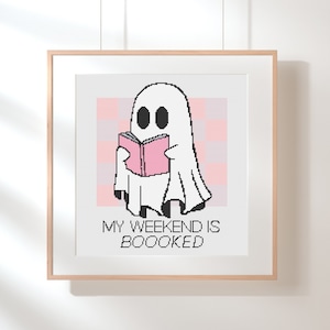 Peut inclure: Un fantôme blanc aux yeux noirs lit un livre rose. Le texte sous le fantôme dit "My weekend is boooked".