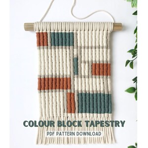 May include: A beige macrame wall hanging with a geometric pattern in shades of teal and orange. The hanging is attached to a wooden dowel rod and has fringe at the bottom. The text "COLOUR BLOCK TAPESTRY PDF PATTERN DOWNLOAD" is printed below the hanging.