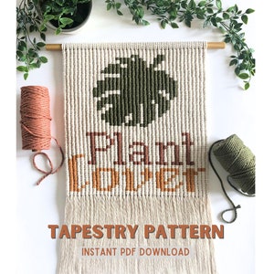 May include: A tapestry pattern featuring a green monstera leaf and the text "Plant Lover" in orange and brown. The pattern is on a white background and is surrounded by beige yarn.