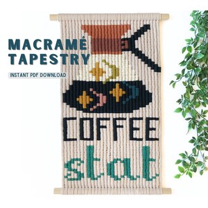 Op de afbeelding: Een macramé wandkleed met een koffiekan ontwerp en de woorden "Coffee Stop" in zwart en turquoise garen. Het wandkleed is gemaakt van natuurlijk gekleurd garen en heeft een houten lat aan de boven- en onderkant.
