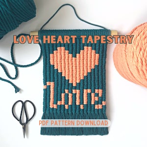 May include: A teal and peach colored yarn wall hanging with the word "LOVE" woven into the design. The hanging features a heart shape and the text "PDF PATTERN DOWNLOAD".