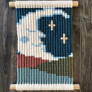 Pode incluir: Uma tape&ccedil;aria de parede feita de fio tecido em tons de creme, azul, verde e marrom. O fio &eacute; tecido em um padr&atilde;o geom&eacute;trico com alguns acentos dourados.