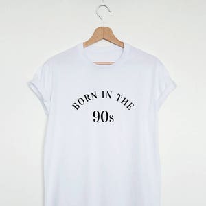 May include: White t-shirt with black text that reads "Born in the 90s".