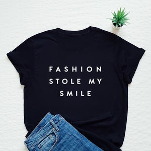 May include: Black t-shirt with white text that reads "FASHION STOLE MY SMILE".