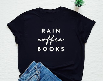 May include: Black t-shirt with white text that reads "RAIN coffee BOOKS". The shirt is laid flat on a white surface with a pair of blue jeans folded next to it.