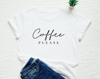 May include: White t-shirt with the text "Coffee Please" in black script font. The shirt is laid flat on a white surface with a pair of blue jeans and a small potted plant.