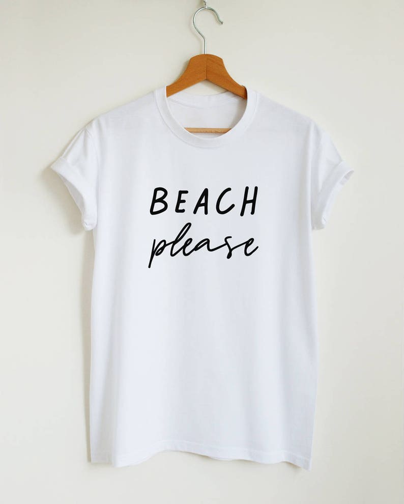 May include: White t-shirt with black text that reads "BEACH please" in a handwritten font.