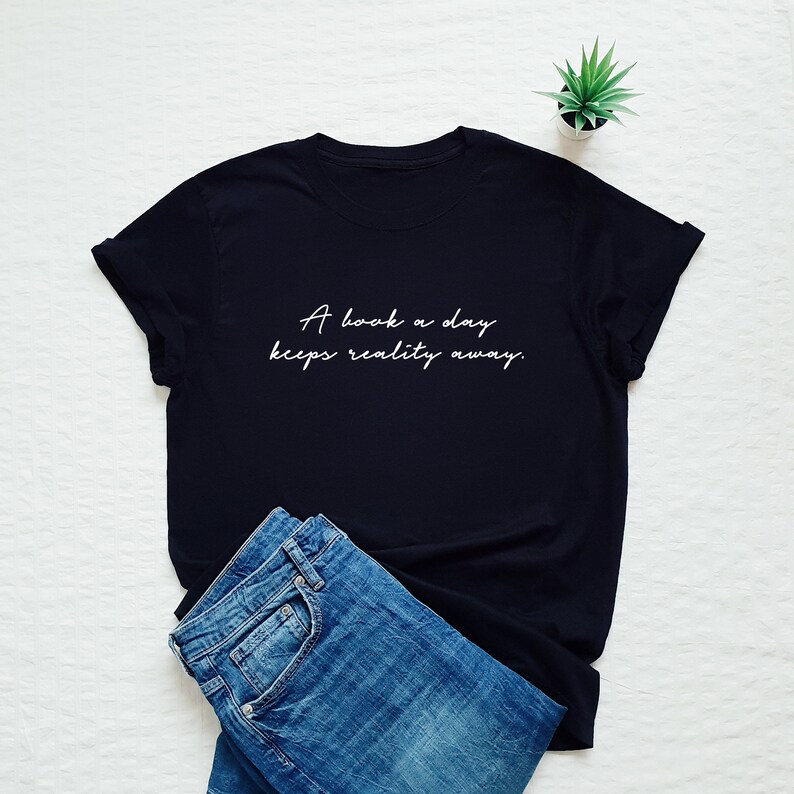 May include: Black t-shirt with white text that reads "A book a day keeps reality away."