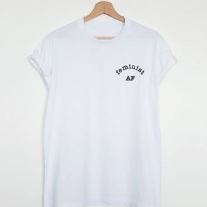 May include: White t-shirt with black text that reads "feminist AF" in an arc.