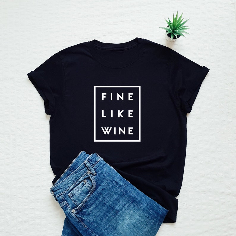 May include: Black t-shirt with white text that reads "FINE LIKE WINE" inside a white square.