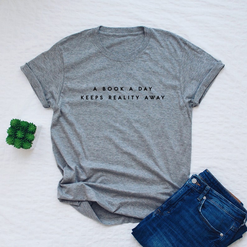 May include: A gray t-shirt with the text "A book a day keeps reality away" printed in black.