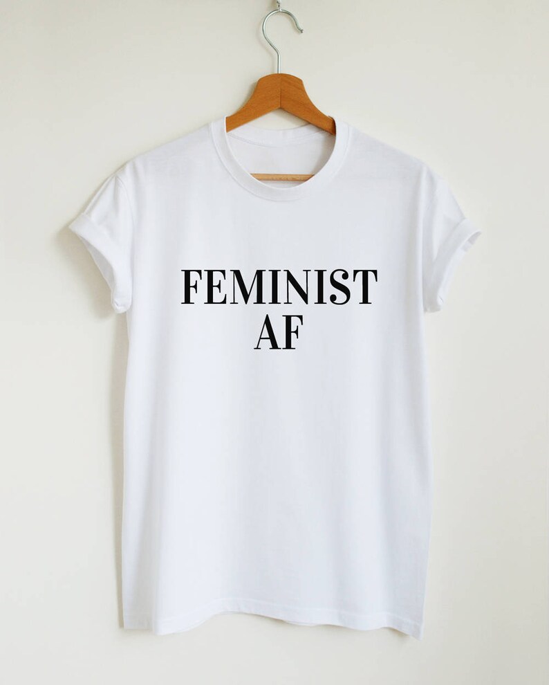 Puede incluir: Camiseta blanca con texto negro que dice "FEMINIST AF".