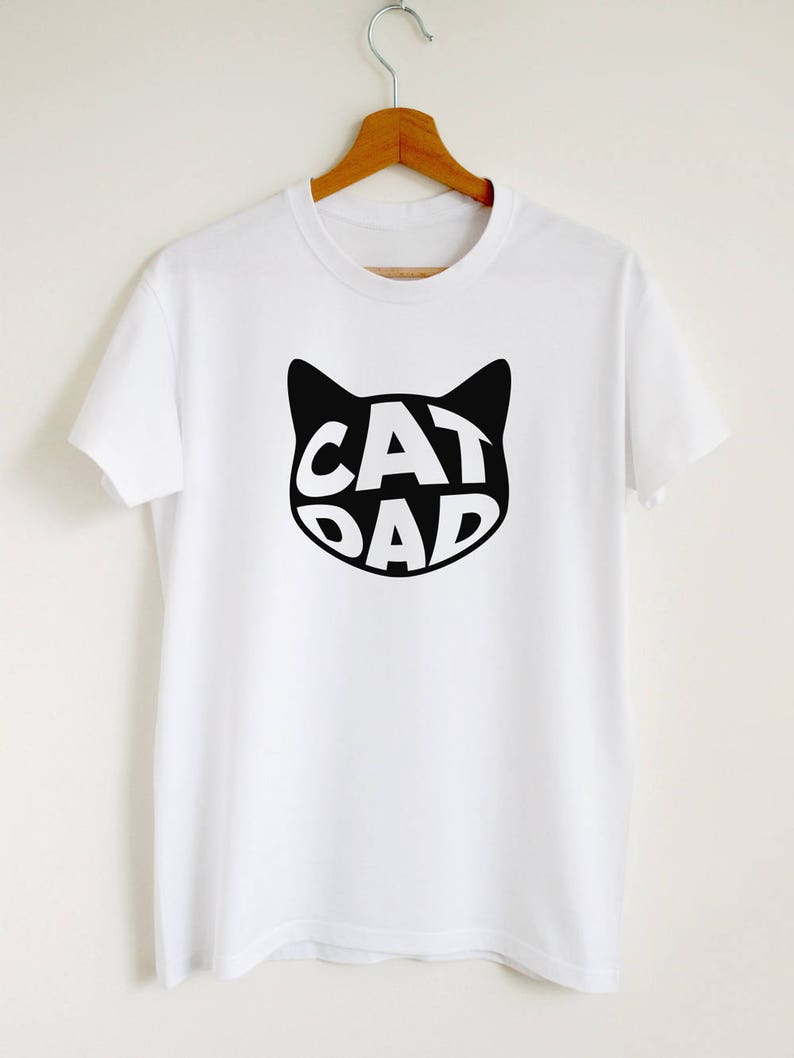 May include: White t-shirt with a black cat silhouette graphic. The word "CAT DAD" is written inside the cat's head.