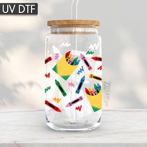 May include: A clear glass jar with a wooden lid and a straw. The jar has a colorful design of crayons and boxes of crayons. The text "Zimbee.com" is on the jar.