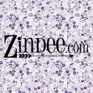 May include: A floral pattern in shades of purple and white. The design features various flowers and foliage. The text "Zindee.com" is displayed in black, with an arrow pointing to the right. The overall theme is a botanical or garden-inspired design.