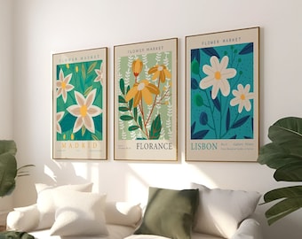 May include: Three framed floral prints with a green, blue, and yellow color scheme. The prints feature stylized flowers and the text "Flower Market" at the top. The cities "Madrid", "Florence", and "Lisbon" are listed below the flowers.