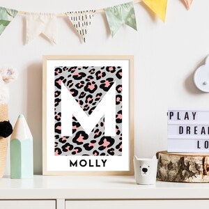 May include: A framed print featuring a white letter M on a pink and black leopard print background. The name Molly is printed below the letter.