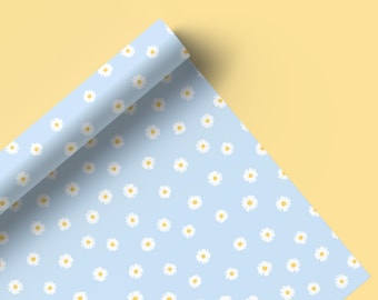 Op de afbeelding: Een rol lichtblauw inpakpapier met een wit madeliefjespatroon. Het papier is opgerold en gedeeltelijk uitgerold, waardoor het patroon zichtbaar wordt.