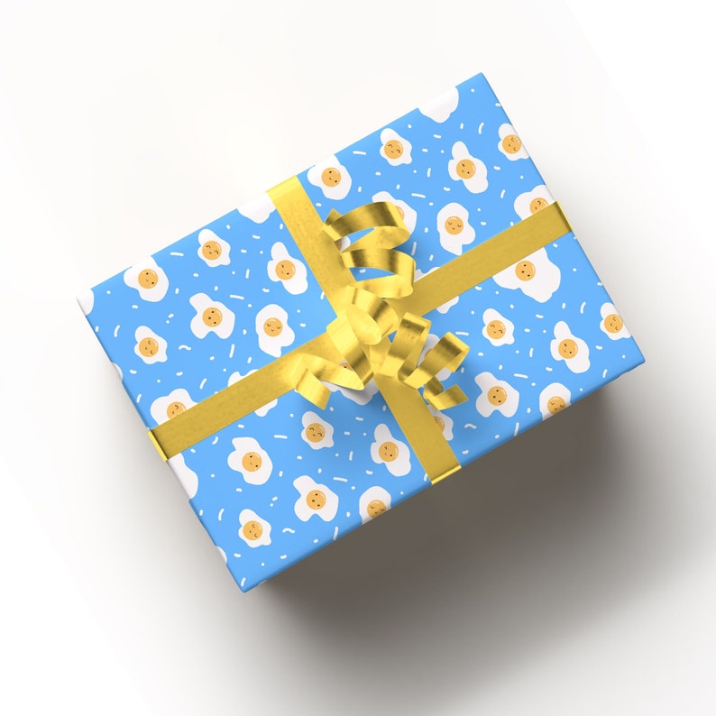 May include: A blue gift box with a yellow ribbon. The box is covered in a pattern of white eggs with yellow yolks on a blue background.