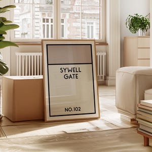 May include: A framed print with a beige and white background. The print features the text "SYWELL GATE NO.102" in black.