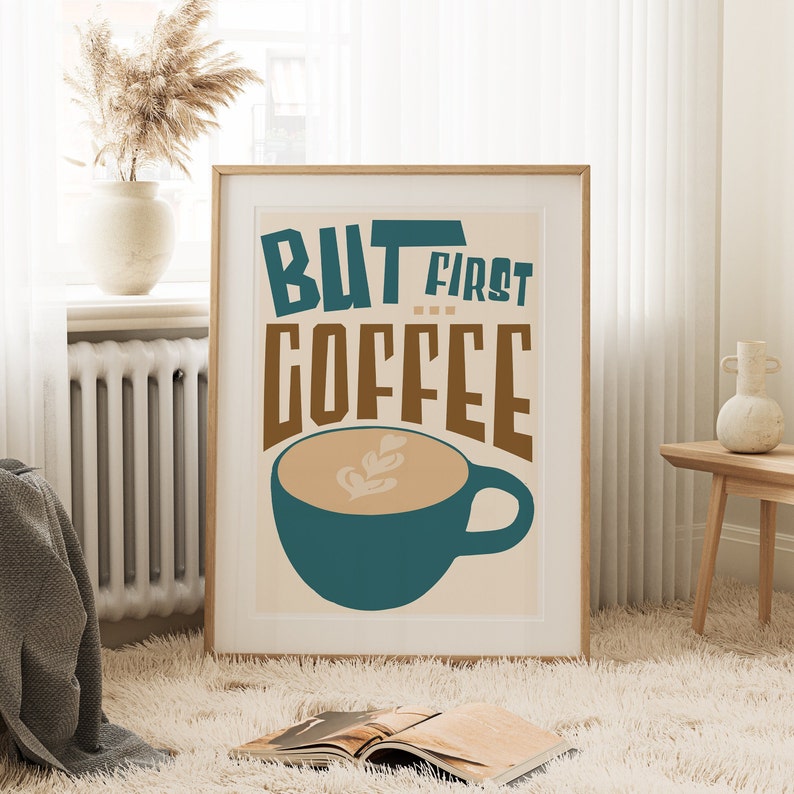 May include: A framed poster with a beige background and the text "But first coffee" in brown and teal lettering. A teal coffee cup with a brown coffee design is below the text.